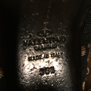 May include: Close-up of the bottom of a black shoe with the text "VALENTINO GARAVANI" and "MADE IN ITALY" in white. The size 35 1/2 is also visible.