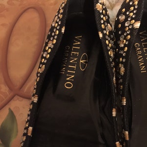 May include: A pair of black flats with gold and silver embellishments. The shoes have the Valentino Garavani logo on the inside.