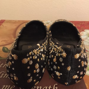 May include: A pair of black flats with gold and white embellishments. The shoes are decorated with small beads and sequins.