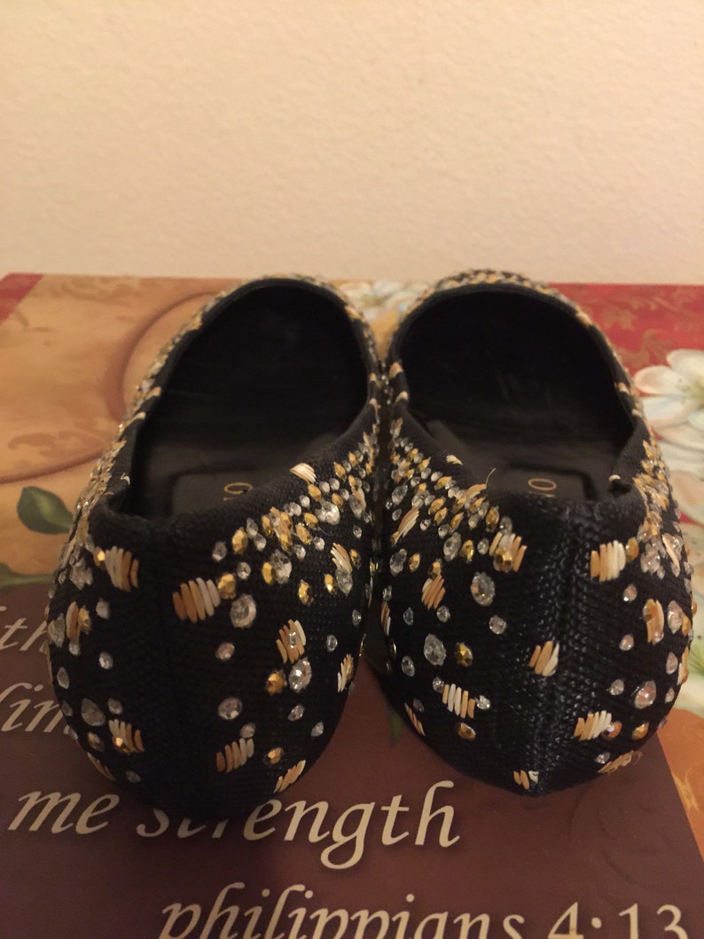 May include: A pair of black flats with gold and white embellishments. The shoes are decorated with small beads and sequins.