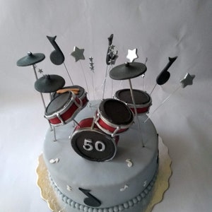May include: A gray and red drum set cake decorated with black musical notes and silver stars. The cake is decorated with the number "50" on the front.