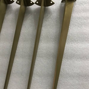 May include: Four gold metal table legs with a triangular top and three holes. The legs are approximately 16 inches tall.