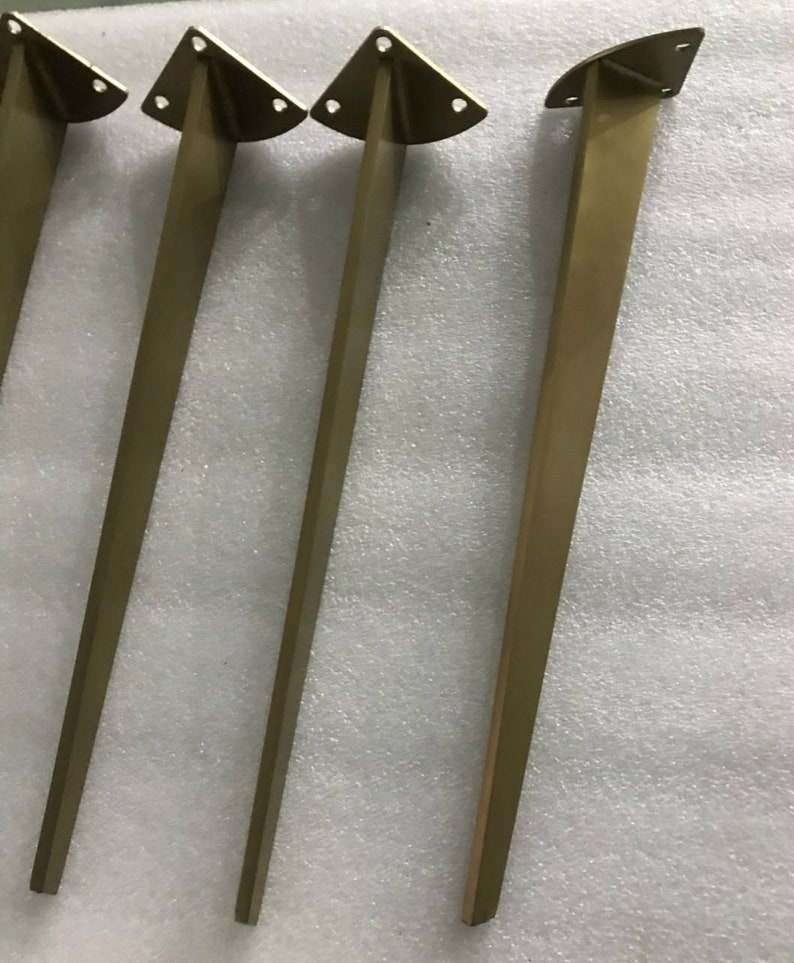May include: Four gold metal table legs with a triangular top and three holes. The legs are approximately 16 inches tall.