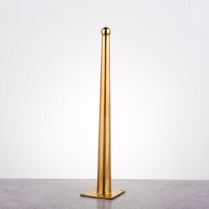 May include: A gold metal furniture leg with a round top and a square base.