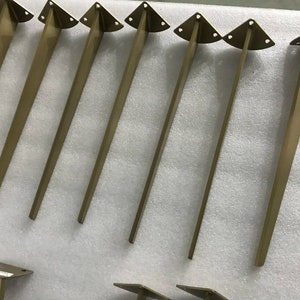 May include: Eight gold metal table legs with a triangular top. The legs are approximately 12 inches long.