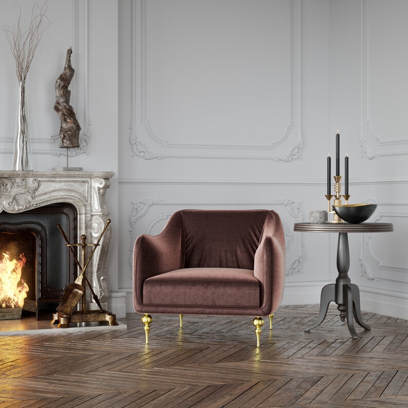 Puede incluir: Un sill&oacute;n de terciopelo marr&oacute;n con patas doradas en una habitaci&oacute;n con chimenea y una peque&ntilde;a mesa auxiliar. La silla tiene respaldo y reposabrazos redondeados. Una mesa negra con borde dorado sostiene un cuenco negro y candelabros.