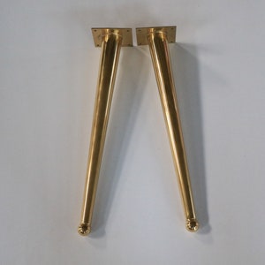 May include: Two gold metal table legs with a rounded top and a square base.