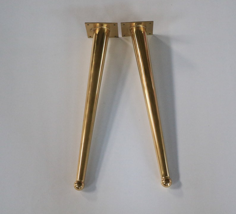May include: Two gold metal table legs with a rounded top and a square base.