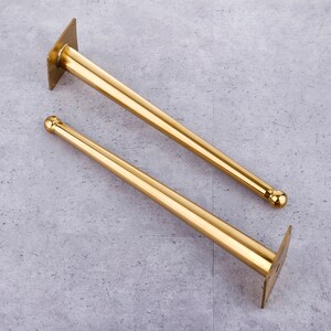 May include: Two gold metal furniture legs with a rounded top and a flat base plate. The legs are approximately 30 cm long.