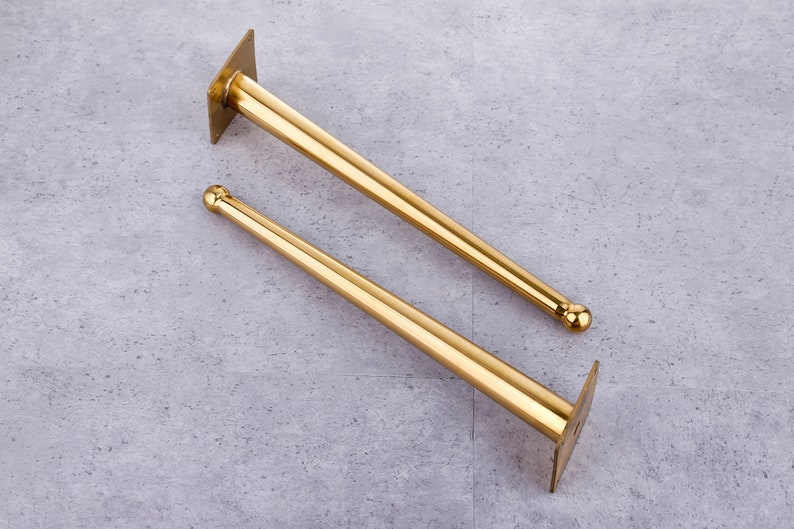 May include: Two gold metal furniture legs with a rounded top and a flat base plate. The legs are approximately 30 cm long.