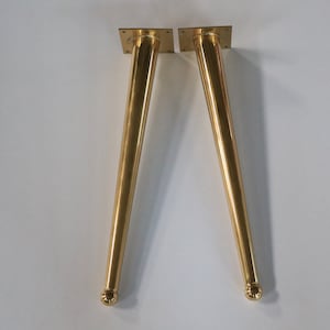 May include: Two gold metal table legs with a rounded top and a square base.