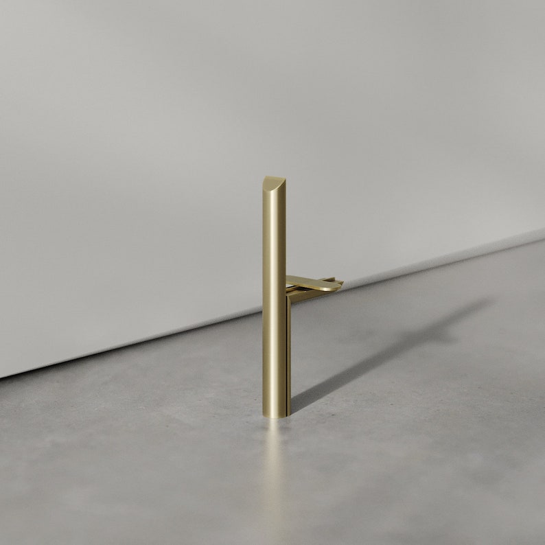 May include: A gold metal door stop with a rounded top and a flat base. The door stop is designed to prevent doors from slamming.