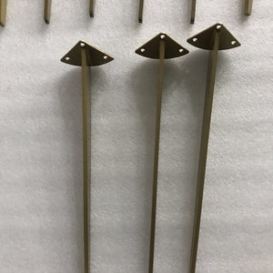 May include: Three gold metal table legs with triangular bases. Each leg has three holes in the base.