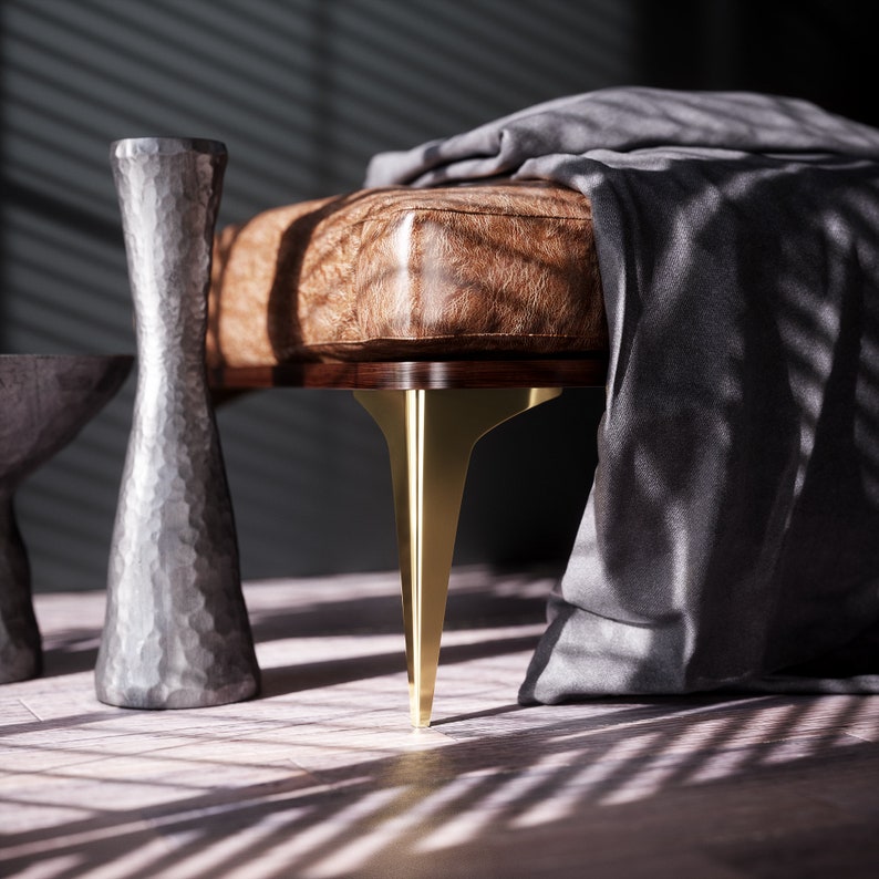 May include: A brown leather bench with gold metal legs. The bench is covered with a gray blanket and is sitting on a wooden floor.