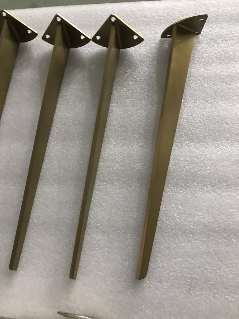 May include: Four gold metal table legs with a triangular top and three holes for mounting.
