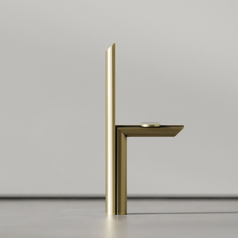 May include: A gold metal faucet with a single handle and a rectangular spout. The faucet is mounted on a white wall.