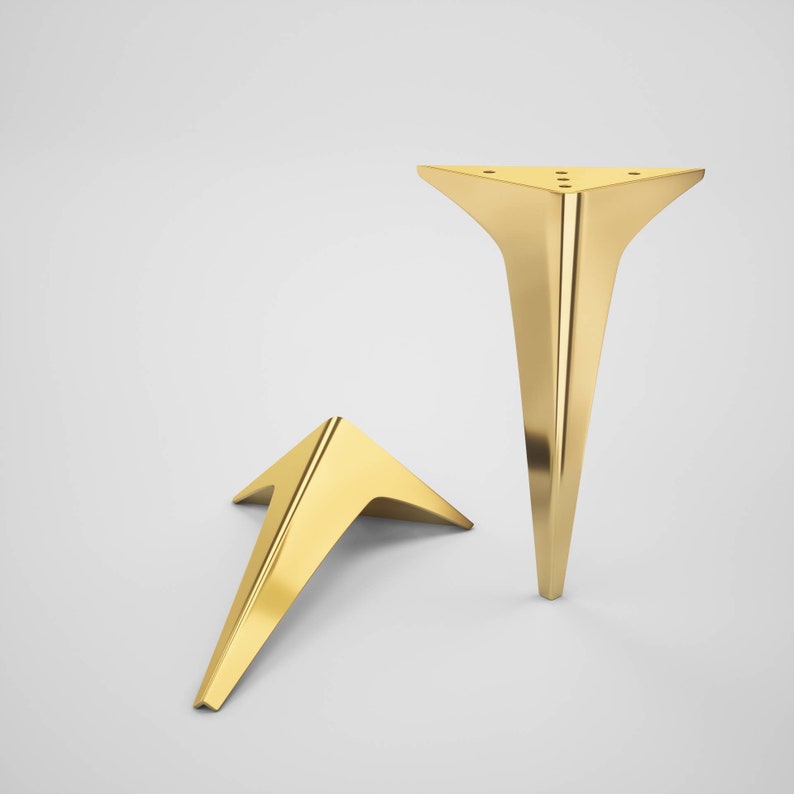 May include: Two gold metal furniture legs in a triangular shape. The legs are angled and have a pointed tip.