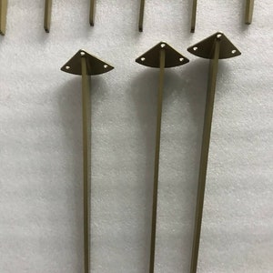 May include: Three gold metal furniture legs with triangular bases. Each leg has three holes in the base.