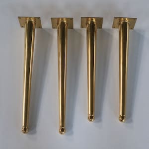 May include: Four gold metal table legs with a square base and a rounded top.