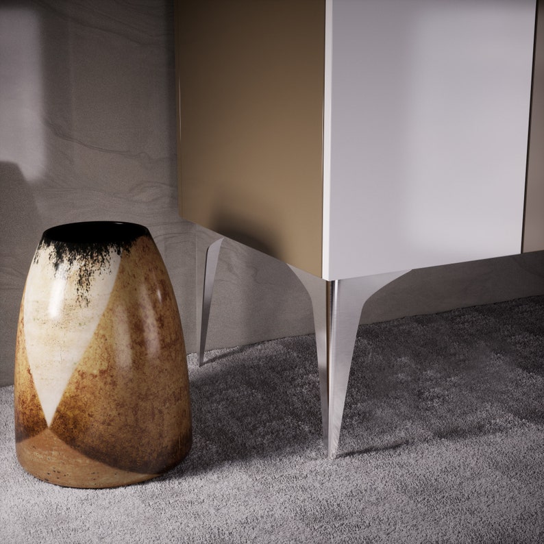 May include: A brown and white ceramic vase with a geometric pattern sits on a carpet in front of a cabinet with white and brown doors and clear acrylic legs.