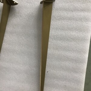 May include: A gold metal table leg with a triangular base. The leg is about 16 inches tall.