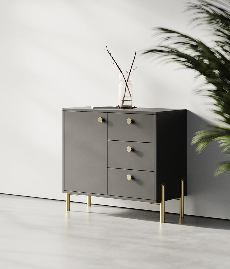 May include: A dark gray cabinet with three drawers and a door. The cabinet has gold metal legs and gold round knobs.