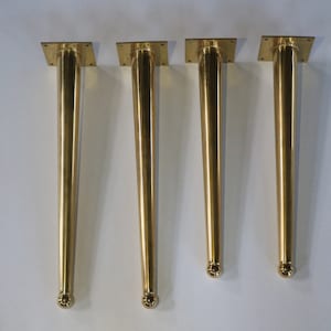 May include: Four gold metal table legs with a rounded top and a square base.