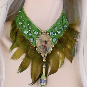May include: A green velvet choker with a gold-toned pendant featuring a vintage illustration of a fairy. The choker is adorned with clear rhinestones and green feathers.