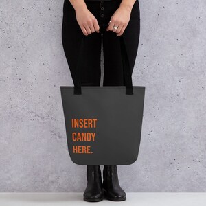Könnte beinhalten: Eine schwarze Tragetasche mit orangefarbenem Text, der "INSERT CANDY HERE." lautet.