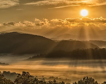May include: A scenic sunrise over a misty valley with rolling hills and sunbeams breaking through the clouds.