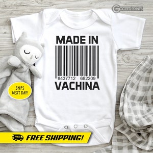 Peut inclure: Combinaison blanche pour bébé avec un texte noir qui dit "MADE IN" avec un code-barres et "VACHINA" en dessous.