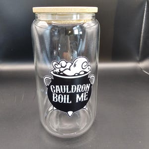 May include: A clear glass jar with a bamboo lid. The jar features a black and white graphic of a cauldron with the text "GAULDRON BOIL ME". The jar is cylindrical and appears to be empty.