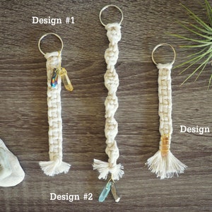May include: Three macrame keychains with different designs. The keychains are made with white cord and feature a variety of crystals and beads. The keychains are labeled "Design #1", "Design #2", and "Design #3".