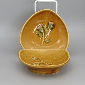Könnte beinhalten: Zwei braune Keramikschalen mit einem erhabenen Design einer grünen Distelblüte. Die Schalen sind übereinander gestapelt.