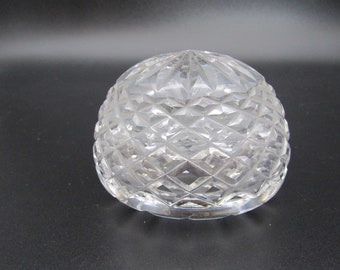 May include: A clear, cut-glass bowl with a diamond pattern. The bowl is dome-shaped and sits on a flat base. The glass is transparent, allowing light to pass through and reflect off the cut facets. The bowl is likely used for decorative purposes.