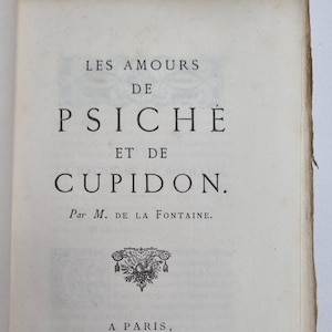 Op de afbeelding: Een vintage boek getiteld "Les Amours de Psyche et de Cupidon" van M. de la Fontaine, uitgegeven in Parijs in 1669. De boekomslag heeft een decoratief ontwerp met een kroon en bloemmotieven.