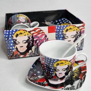 May include: A set of ceramic teacups and saucers featuring a pop art design of a blonde woman with red lips, set against a backdrop of the American flag. The set includes a spoon and is packaged in a decorative box.