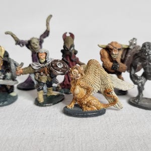 Puede incluir: Colección de figuras en miniatura de fantasía. Las figuras incluyen una esfinge alada, un minotauro, un humanoide con cuernos, un guerrero con escudo y otros monstruos. Las figuras están pintadas con varios colores y detalles.