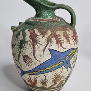 Può includere: Brocca in ceramica con manico e beccuccio verdi. Il corpo è bianco sporco con disegni dipinti di un delfino blu, palme e altre creature marine. Il bordo e il manico sono verdi con accenti rossi.
