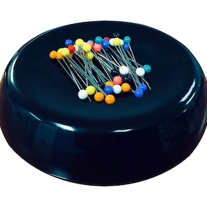 May include: A black magnetic pincushion with a variety of colorful pins. The pins are arranged in a random pattern on the pincushion.