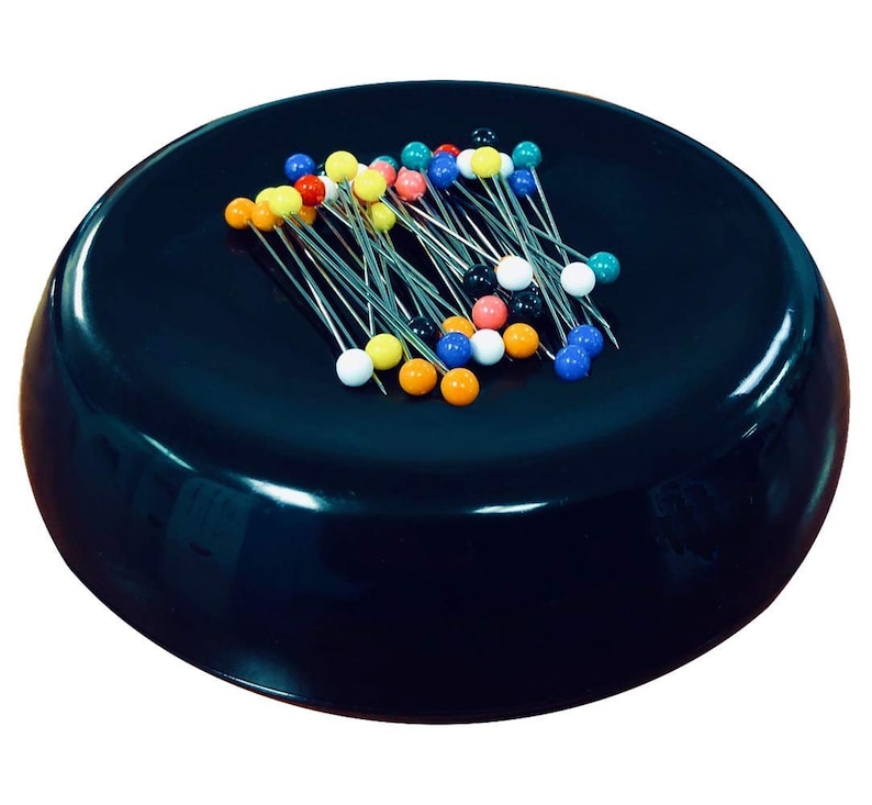 May include: A black magnetic pincushion with a variety of colorful pins. The pins are arranged in a random pattern on the pincushion.