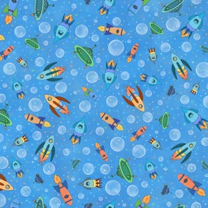 May include: A whimsical pattern featuring cartoon rockets, UFOs, bubbles, and stars on a blue background. The rockets are in various colors, including orange, blue, and green, with flames and detailed designs. The overall theme is space and fantasy.