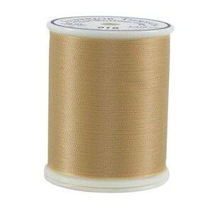 May include: A spool of Superior Threads brand thread, in a light tan color. The thread is tightly wound around a white plastic spool. The label on top of the spool is white with blue text.
