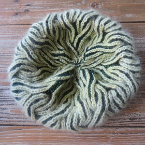 Peut inclure: Un chapeau tricoté avec un motif rayé dans les tons de vert et crème. Le chapeau est fait d'un fil doux et moelleux.
