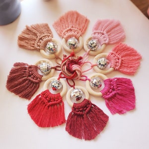 May include: Nine wooden rings with a silver disco ball charm, each ring is tied with a tassel in shades of pink and red.