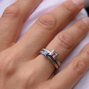 Puede incluir: Un anillo de plata con dos piedras preciosas de forma cuadrada. La piedra m&aacute;s grande es rosa y la m&aacute;s peque&ntilde;a es azul.