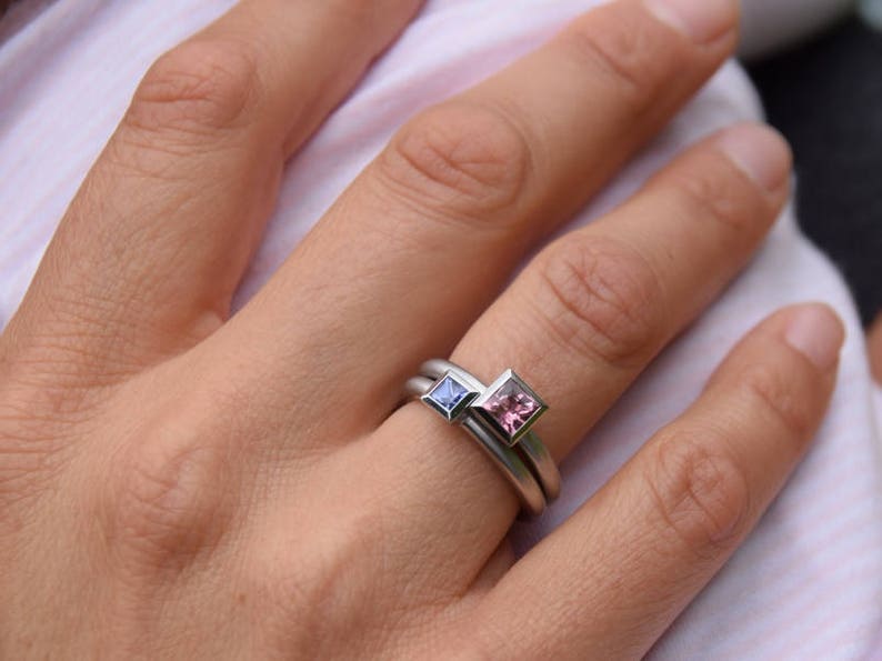 Puede incluir: Un anillo de plata con dos piedras preciosas de forma cuadrada. La piedra m&aacute;s grande es rosa y la m&aacute;s peque&ntilde;a es azul.