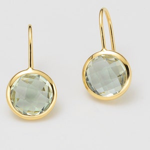 Puede incluir: Un par de pendientes de oro con piedras preciosas redondas verdes. Los pendientes tienen un diseño simple y elegante.