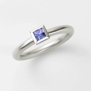 Puede incluir: Un anillo de plata con una peque&ntilde;a piedra preciosa cuadrada de color p&uacute;rpura engastada en un engaste de plata.