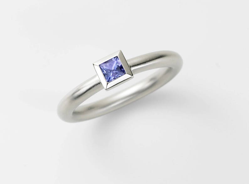 Puede incluir: Un anillo de plata con una peque&ntilde;a piedra preciosa cuadrada de color p&uacute;rpura engastada en un engaste de plata.
